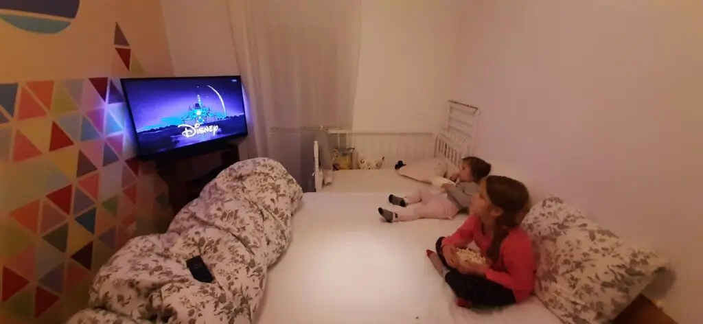 How to Paint Baby Room Wall 13 Two children watch a Disney movie on TV while relaxing on a bed in a cozy kids bedroom.