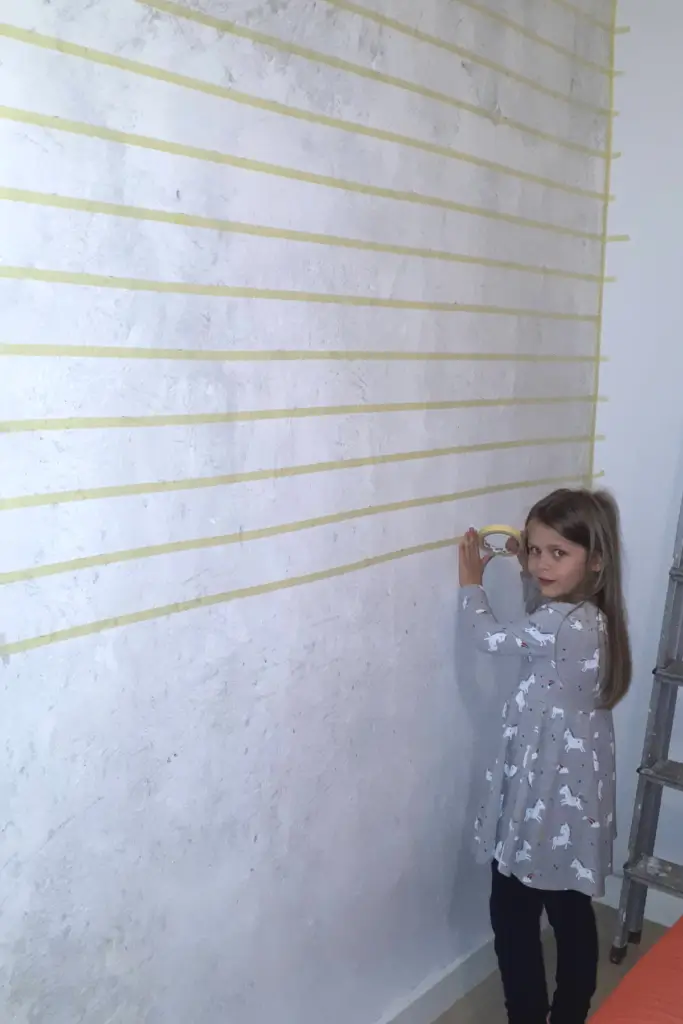 How to Paint Baby Room Wall 9 Girl applying horizontal masking tape lines on a white wall for DIY painting project