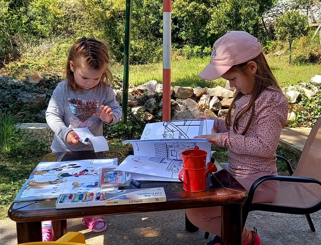 How to Deal with Toddlers Fighting Over Toys 2 Two children coloring and crafting at an outdoor table with crayons and activity books in a sunny garden