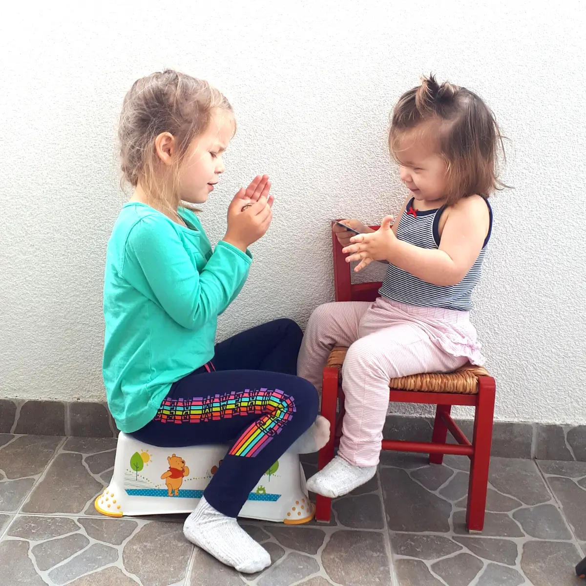 How to Deal with Toddlers Fighting Over Toys 6 Two young children playing a hand-clapping game indoors on small chairs, smiling during playtime