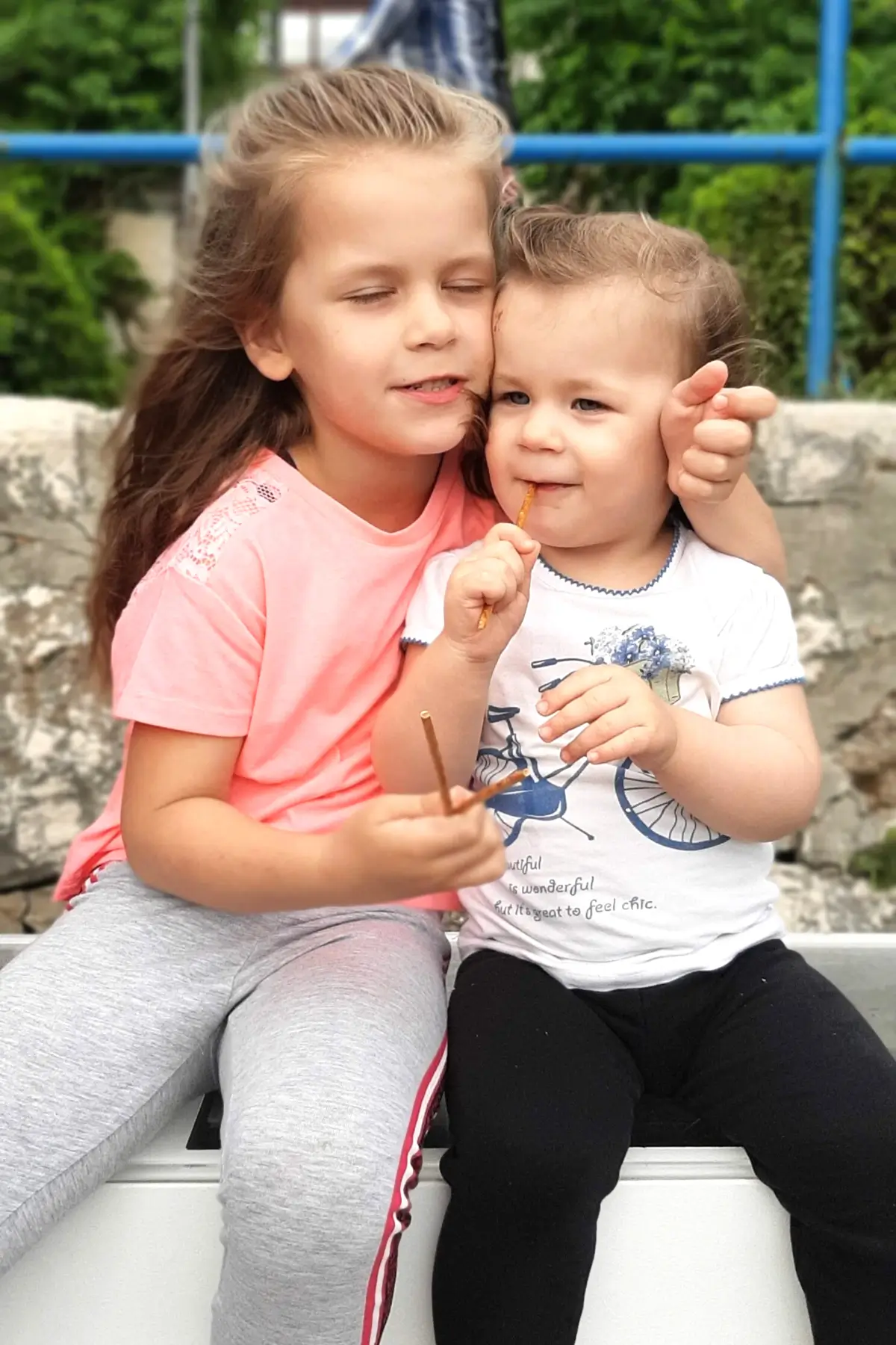 How to Deal with Toddlers Fighting Over Toys 4 Two young children hugging on a bench, smiling and eating pretzel sticks outdoors