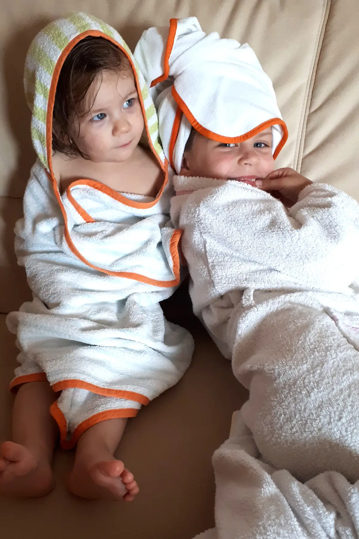 How to Deal with Toddlers Fighting Over Toys 5 Two toddlers wrapped in hooded bath towels, smiling and cozy after bath time on a beige sofa