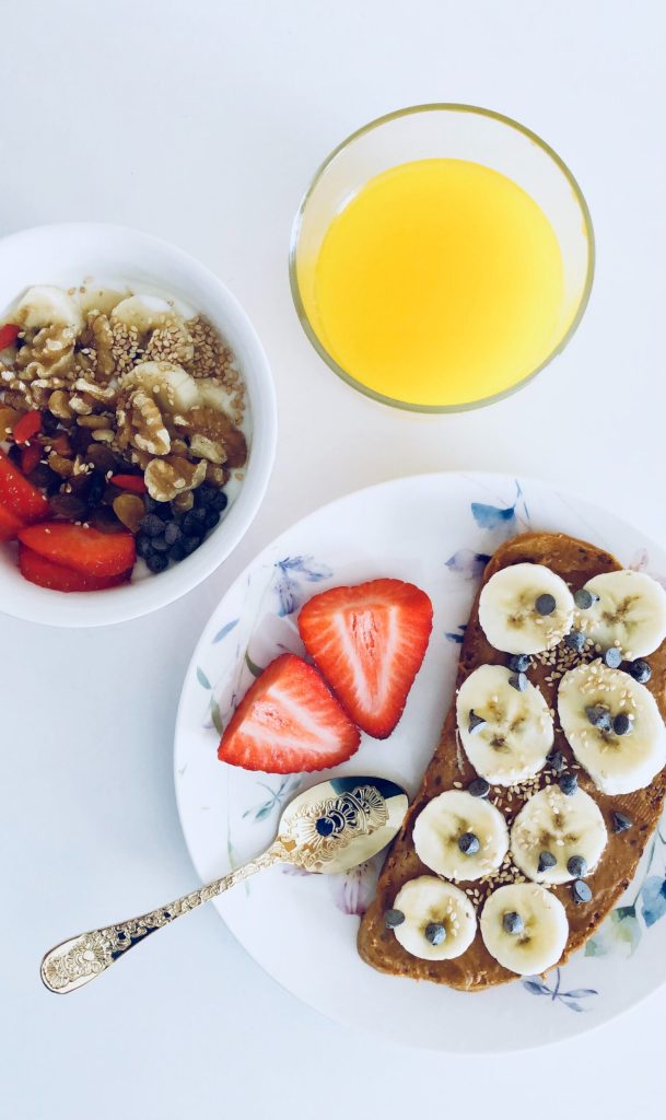 Healthy breakfast: nut butter banana toast, strawberries, yogurt parfait, and orange juice