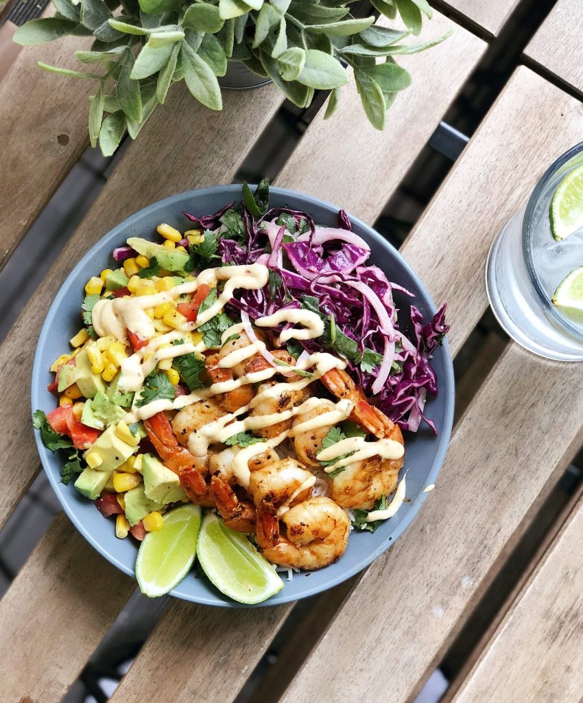 Grilled shrimp bowl with avocado, corn, red cabbage slaw, cilantro and lime wedges