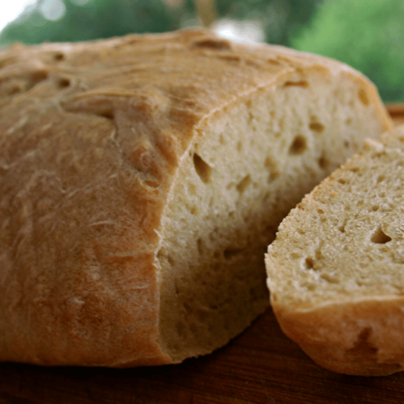 Crusty artisan bread loaf with one slice on a wooden cutting board