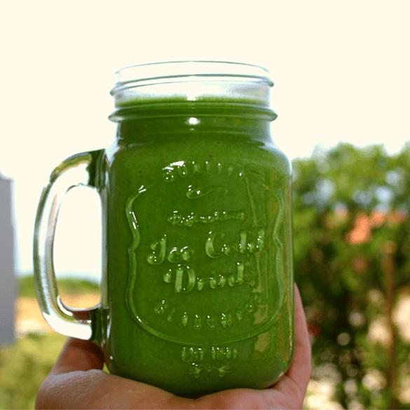 Hand holding a healthy green smoothie in a mason jar outdoors