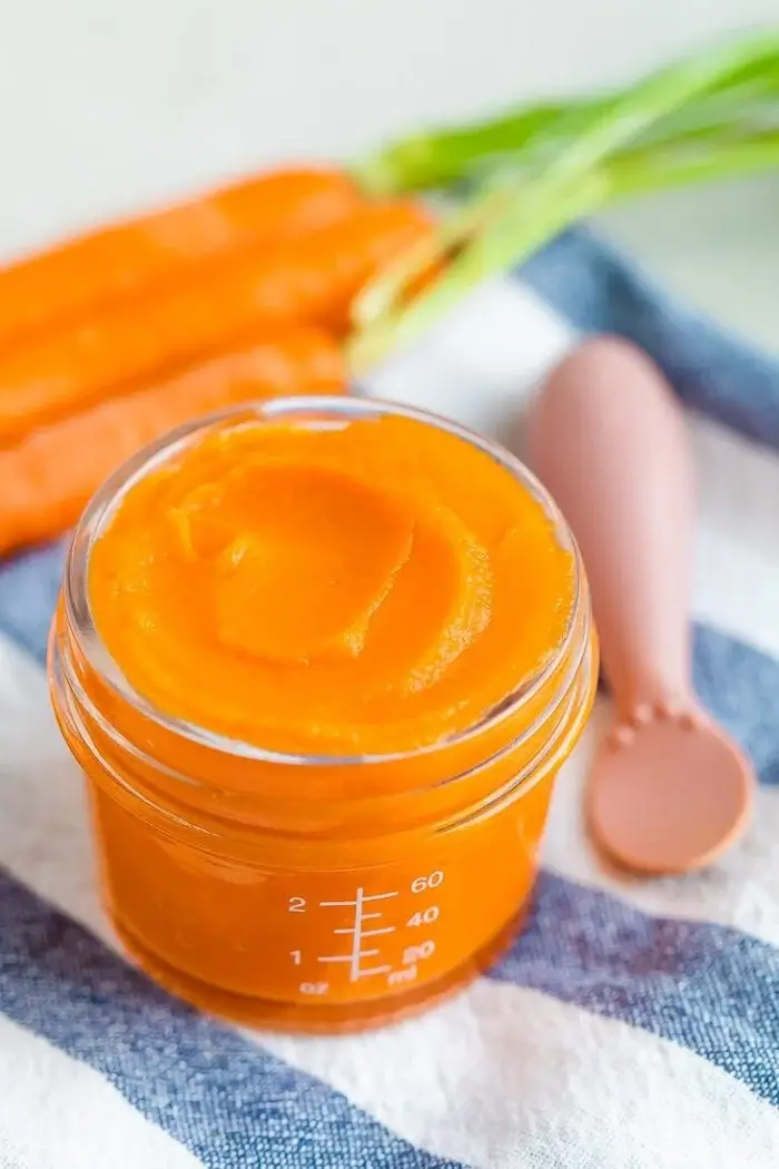 Homemade carrot puree baby food in a jar with fresh carrots and spoon