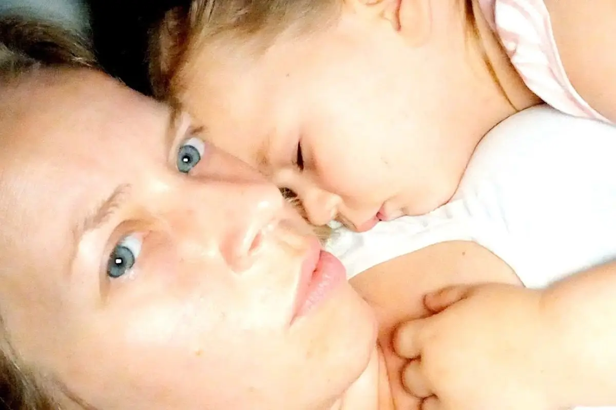 About 12 Mother and child cuddling in bed, toddler asleep on mom's chest